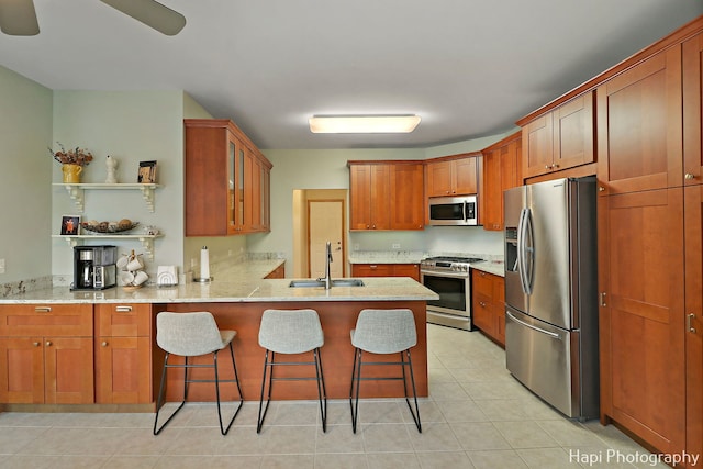 kitchen featuring sink, stainless steel appliances, light stone counters, kitchen peninsula, and a breakfast bar