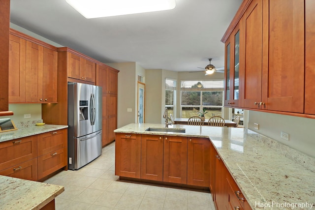 kitchen with stainless steel fridge with ice dispenser, sink, ceiling fan, and light stone counters