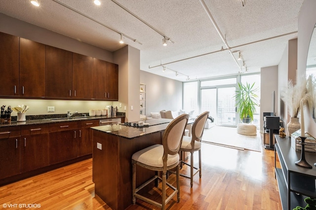 kitchen featuring a kitchen breakfast bar, light wood-type flooring, expansive windows, dark stone counters, and a center island