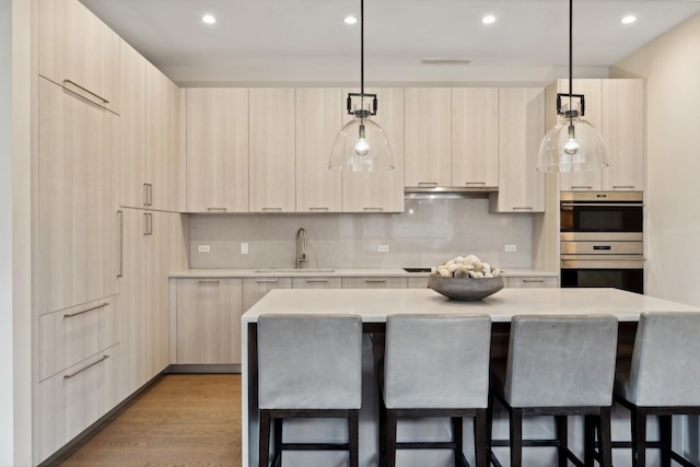 kitchen with sink, a large island, light brown cabinetry, and hanging light fixtures