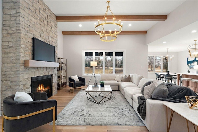 living room featuring beamed ceiling, a fireplace, a chandelier, and light hardwood / wood-style flooring