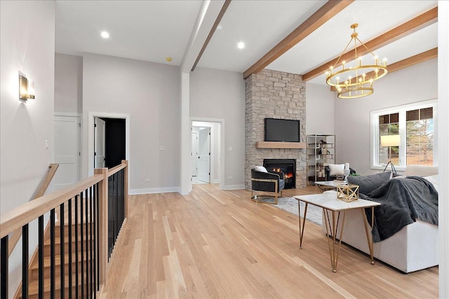 living room featuring beam ceiling, a stone fireplace, wood-type flooring, and an inviting chandelier