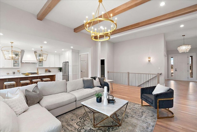 living room with an inviting chandelier, sink, beam ceiling, and light hardwood / wood-style floors