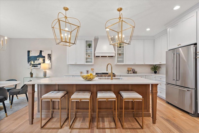 kitchen with an island with sink, custom range hood, high end refrigerator, and a notable chandelier