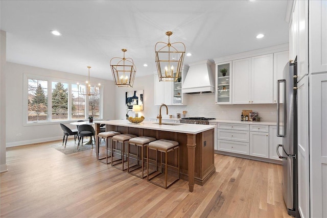 kitchen featuring pendant lighting, a kitchen island with sink, white cabinetry, stainless steel appliances, and custom exhaust hood