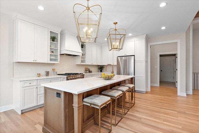 kitchen with pendant lighting, an island with sink, a breakfast bar area, custom exhaust hood, and range