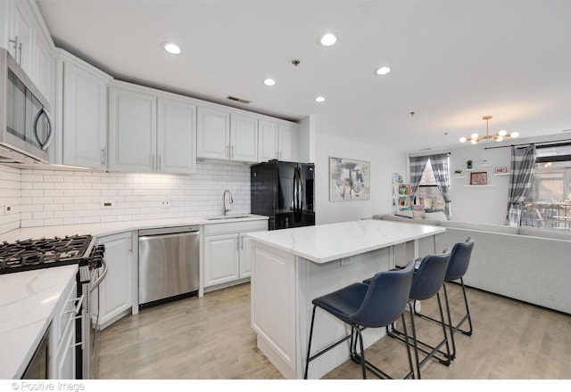 kitchen featuring stainless steel appliances, sink, white cabinets, a center island, and light hardwood / wood-style floors