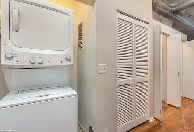 laundry room with light wood-type flooring and stacked washer / drying machine