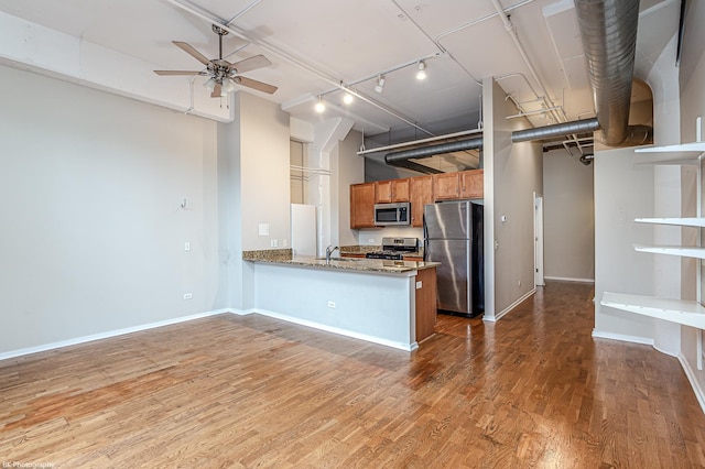 kitchen with stone counters, hardwood / wood-style flooring, ceiling fan, appliances with stainless steel finishes, and kitchen peninsula