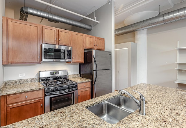 kitchen featuring stainless steel appliances, light stone counters, and sink