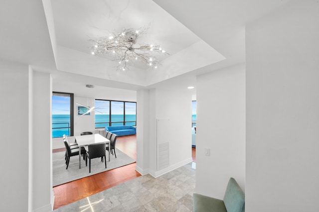 dining area with a raised ceiling, light hardwood / wood-style floors, a water view, and an inviting chandelier