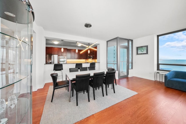 dining area with a water view, wood-type flooring, and a wall of windows