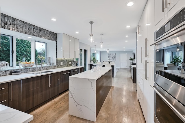 kitchen with dark brown cabinetry, white cabinetry, light stone countertops, sink, and decorative light fixtures