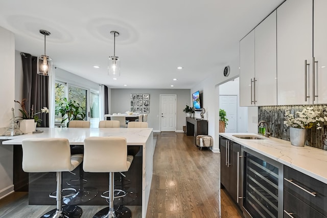 kitchen with white cabinetry, sink, hanging light fixtures, beverage cooler, and a breakfast bar