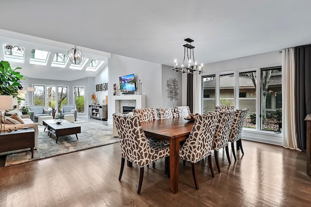 dining space with hardwood / wood-style floors, vaulted ceiling with skylight, and an inviting chandelier