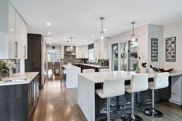 kitchen featuring sink, wall chimney exhaust hood, hanging light fixtures, a kitchen island, and white cabinets