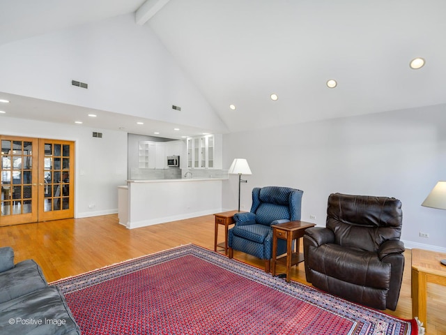 living room featuring beam ceiling, light wood-type flooring, high vaulted ceiling, and french doors