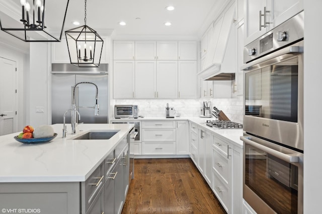 kitchen featuring light stone countertops, appliances with stainless steel finishes, pendant lighting, a center island with sink, and white cabinets