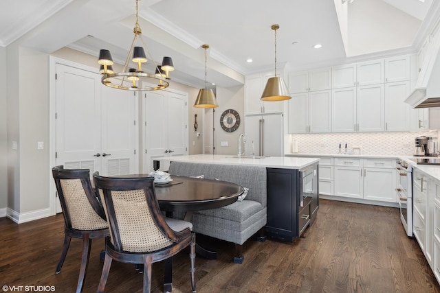 kitchen with pendant lighting, white appliances, a center island with sink, tasteful backsplash, and white cabinetry