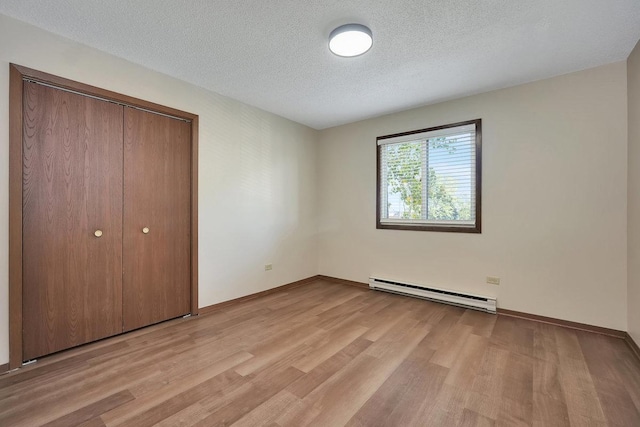 unfurnished bedroom with a textured ceiling, light hardwood / wood-style floors, baseboard heating, and a closet