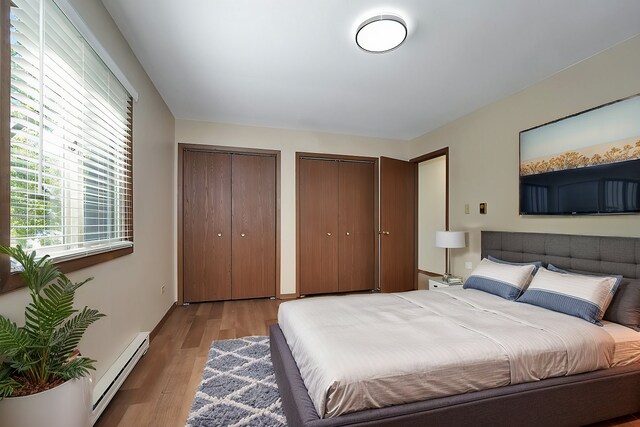 bedroom with two closets, light hardwood / wood-style flooring, and a baseboard radiator