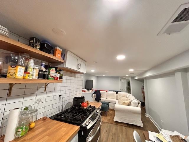 kitchen with butcher block counters, stainless steel gas range oven, dark hardwood / wood-style flooring, decorative backsplash, and white cabinets