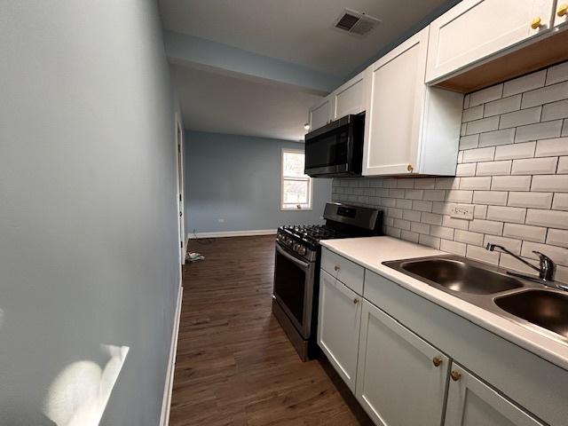 kitchen with white cabinets, sink, stainless steel gas stove, dark hardwood / wood-style floors, and decorative backsplash