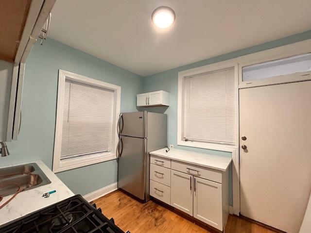 kitchen with stainless steel fridge, light hardwood / wood-style flooring, white cabinetry, and sink