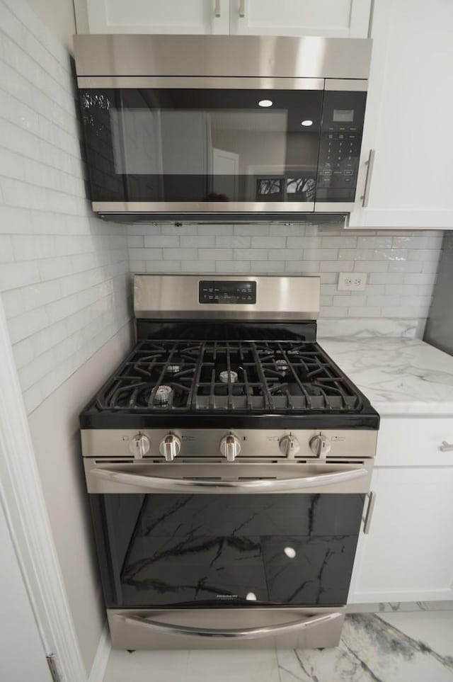 kitchen featuring tasteful backsplash, stainless steel appliances, white cabinetry, and light stone counters