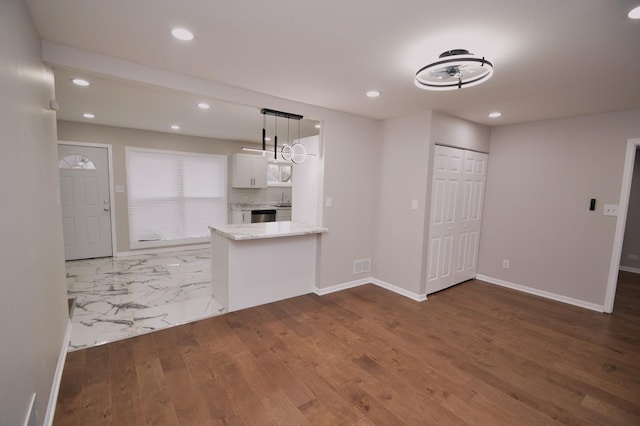 kitchen with white cabinetry, kitchen peninsula, tasteful backsplash, light stone counters, and pendant lighting