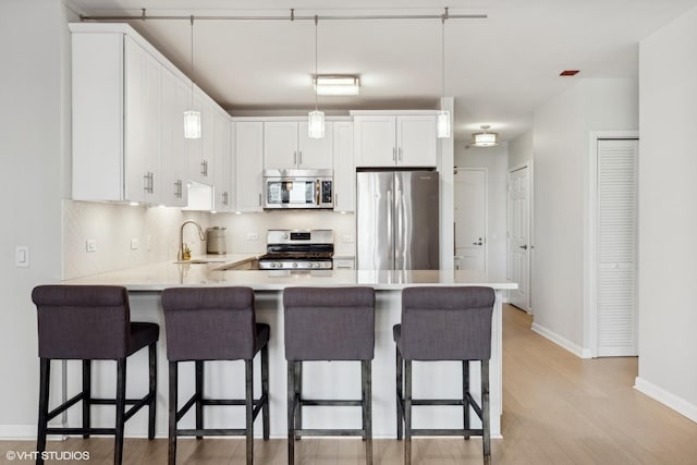 kitchen featuring a breakfast bar, sink, white cabinetry, hanging light fixtures, and stainless steel appliances