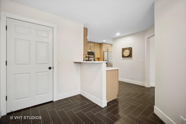 kitchen featuring a breakfast bar area, kitchen peninsula, light brown cabinets, and stainless steel appliances