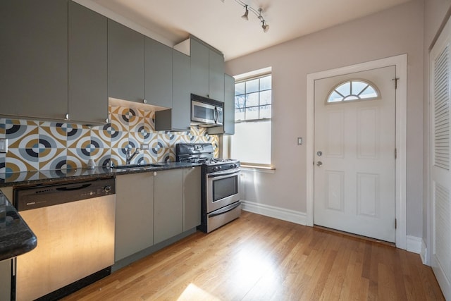 kitchen featuring decorative backsplash, light wood-type flooring, stainless steel appliances, dark stone countertops, and gray cabinets