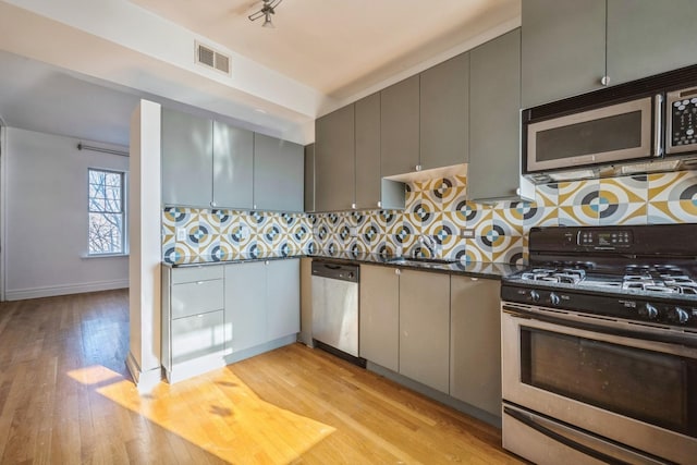 kitchen featuring tasteful backsplash, dark stone countertops, gray cabinets, appliances with stainless steel finishes, and light wood-type flooring