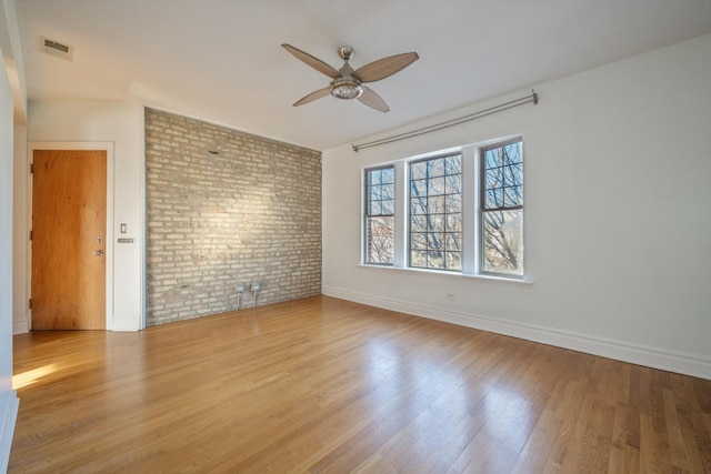 unfurnished room with ceiling fan, light wood-type flooring, and brick wall