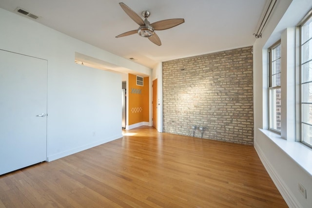 unfurnished room featuring ceiling fan, light hardwood / wood-style flooring, and brick wall