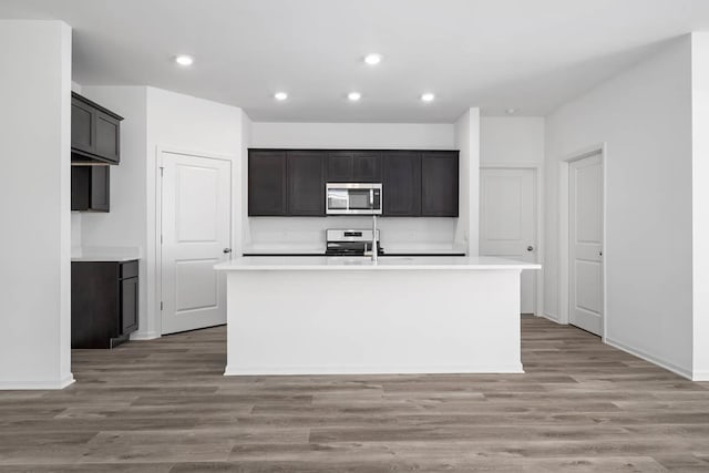 kitchen with range, a center island with sink, light hardwood / wood-style flooring, and dark brown cabinets