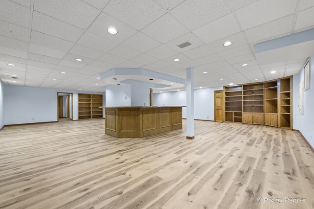 interior space featuring built in shelves, light wood-type flooring, and a drop ceiling