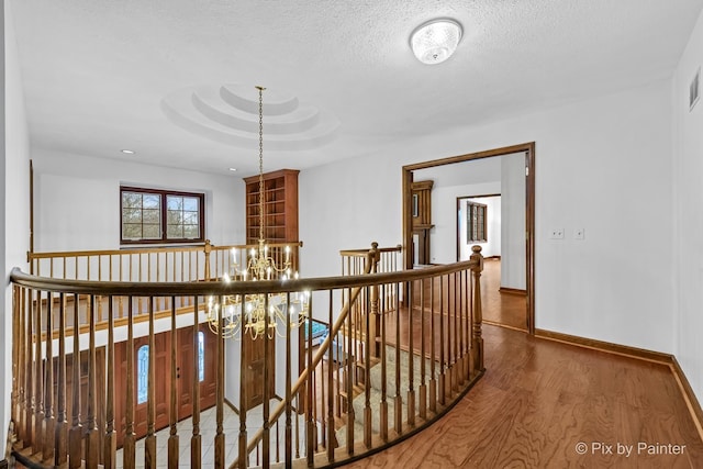 corridor featuring hardwood / wood-style floors, a textured ceiling, and a chandelier