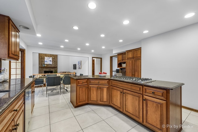 kitchen featuring a kitchen island, dark stone countertops, stainless steel gas cooktop, and a brick fireplace