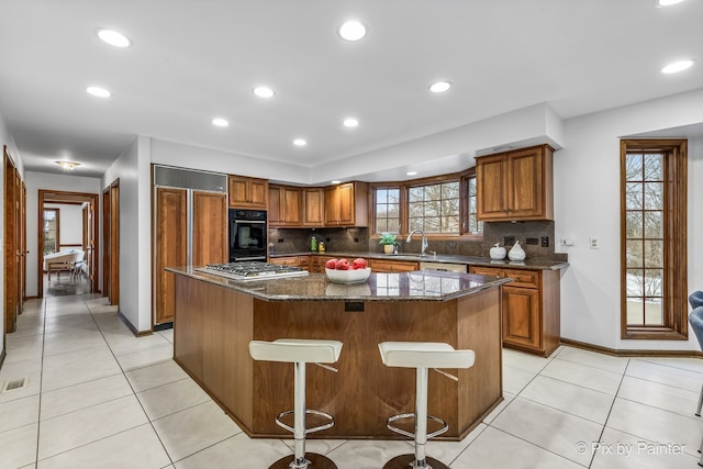 kitchen with a center island, sink, dark stone countertops, a breakfast bar area, and stainless steel gas cooktop