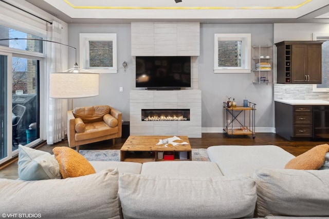 living room featuring a tray ceiling, dark wood-type flooring, and a tiled fireplace