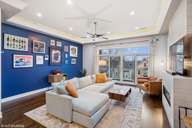 living room with dark hardwood / wood-style flooring, a tray ceiling, and ceiling fan