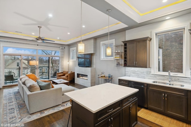 kitchen with sink, decorative light fixtures, a tray ceiling, a tiled fireplace, and a kitchen island