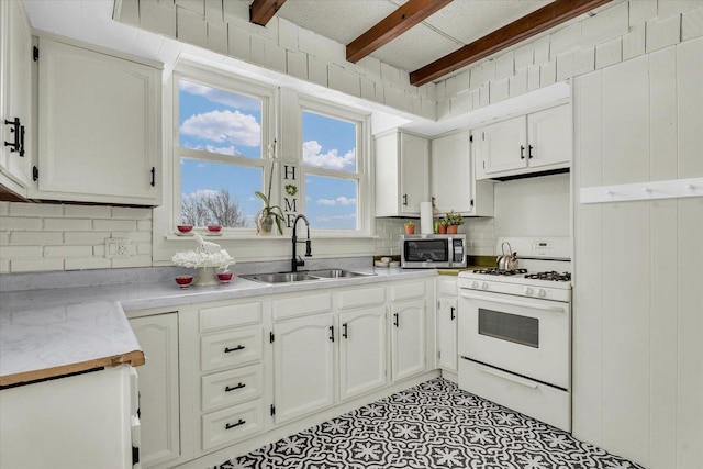 kitchen featuring white range with gas cooktop, sink, white cabinets, and beamed ceiling