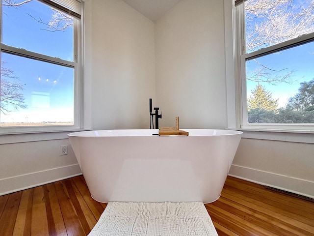 bathroom with a tub to relax in and wood-type flooring