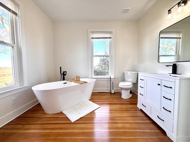 bathroom featuring toilet, wood-type flooring, a bath, and vanity