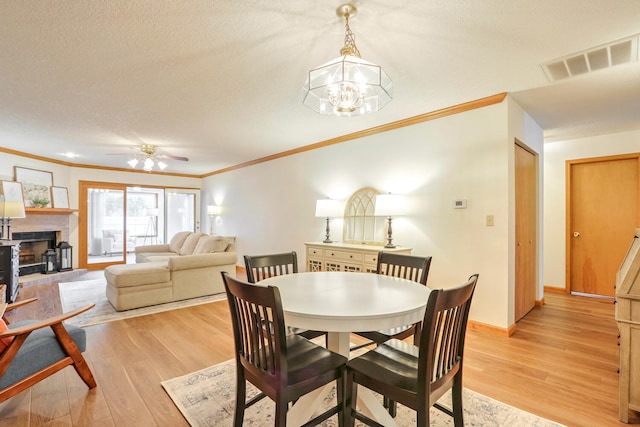 dining space with ceiling fan with notable chandelier, ornamental molding, light hardwood / wood-style floors, and a textured ceiling