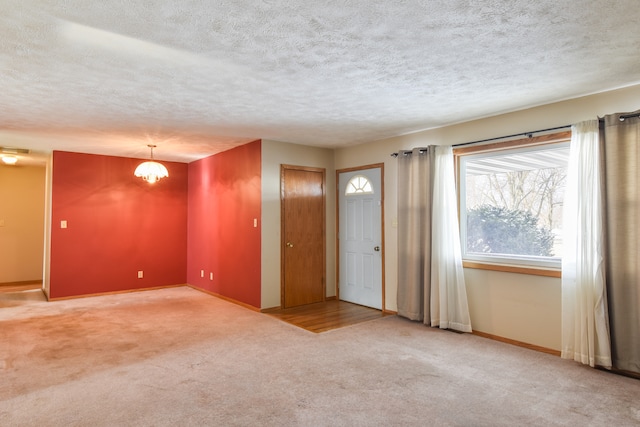 carpeted empty room with a textured ceiling and a notable chandelier