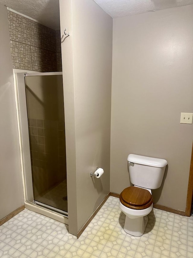 bathroom featuring a textured ceiling, a shower with shower door, and toilet